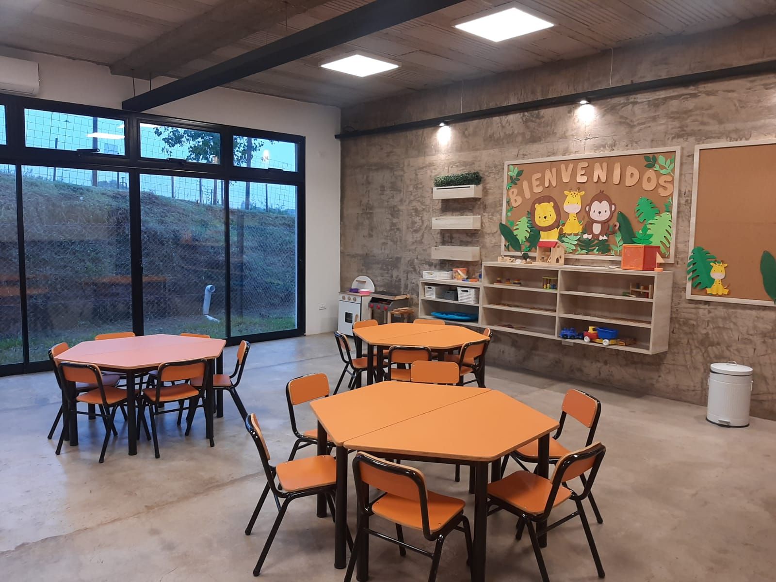 Sala de jardín de infantes equipada con mesas hexagonales naranjas y sillas apilables de Alconche Amoblamientos