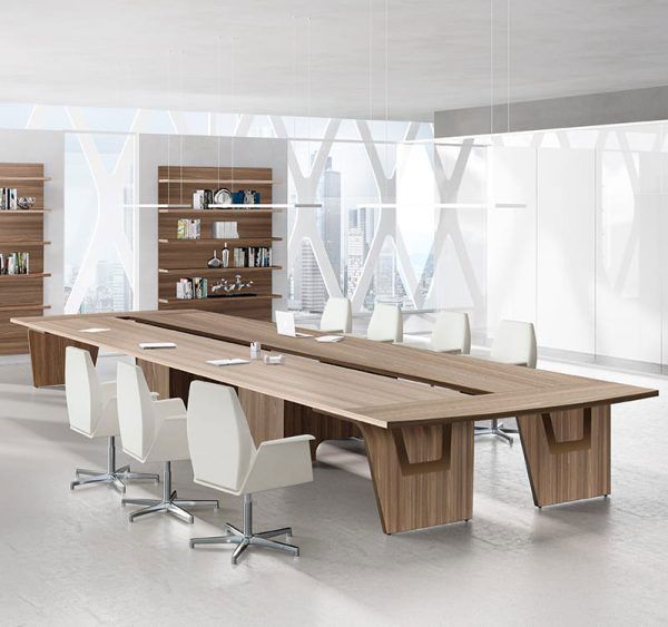 Mesa de sala de juntas en madera con sillas blancas y libreros al fondo, en oficina corporativa
