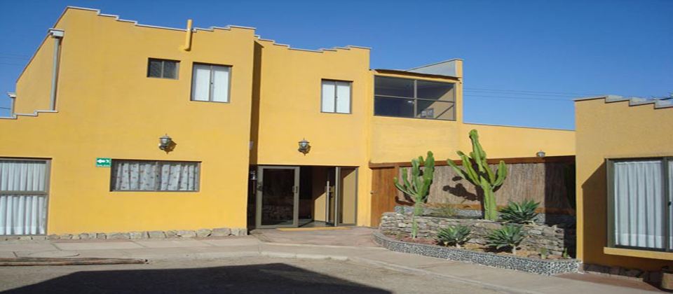 Fachada de Atacama Lodge en adobe amarillo con puerta de madera artesanal y jardín de cactus
