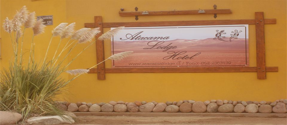 Letrero de bienvenida de Atacama Lodge Hotel entre plumeros del desierto, en la fachada del hotel