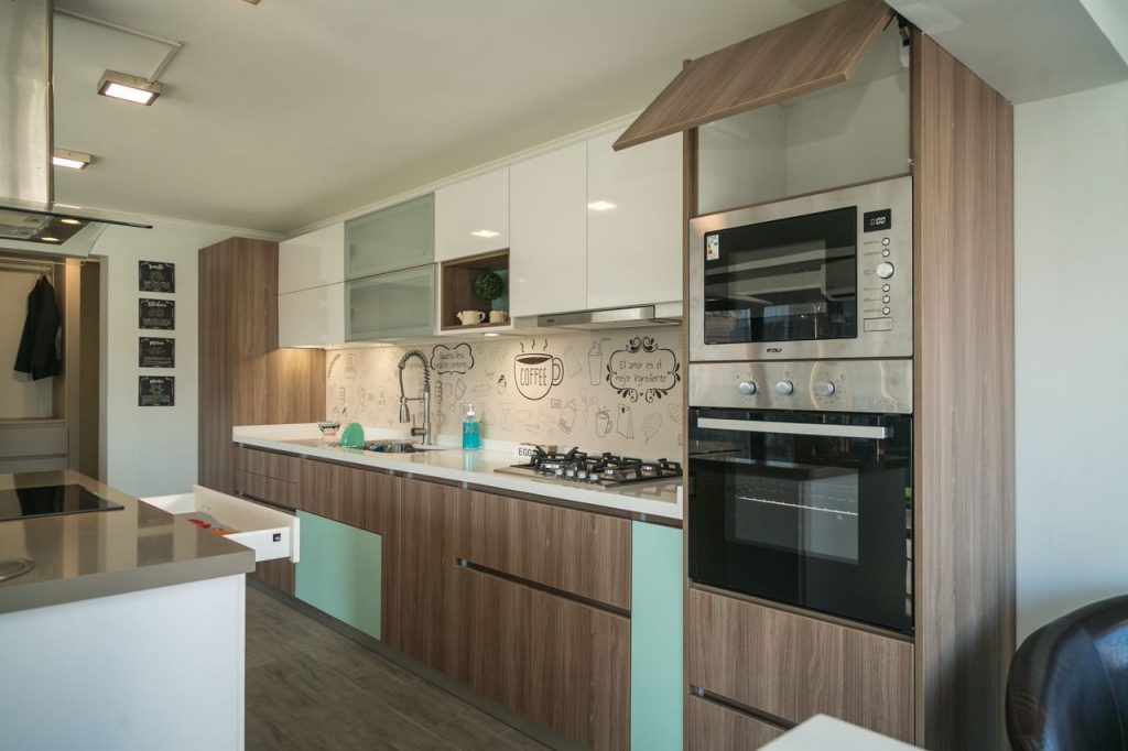 Cocina integral a medida con torre de horno empotrado y muebles en tonos madera, fabricada por Chilemuebles