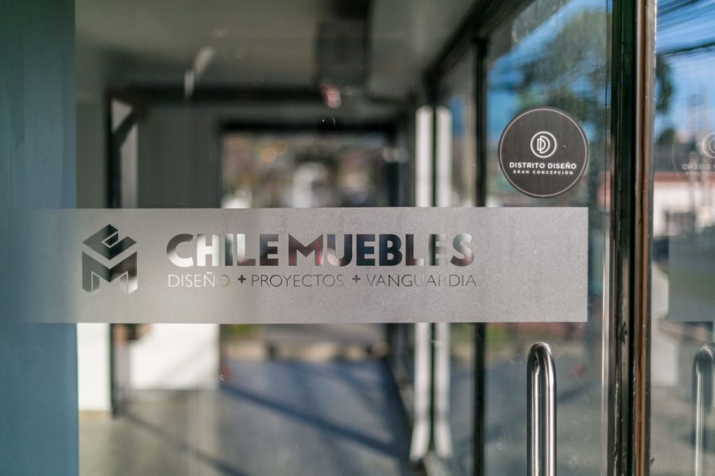 Letrero de vidrio con el logo Chilemuebles y el sello Distrito Diseño Gran Concepción, en la entrada del showroom