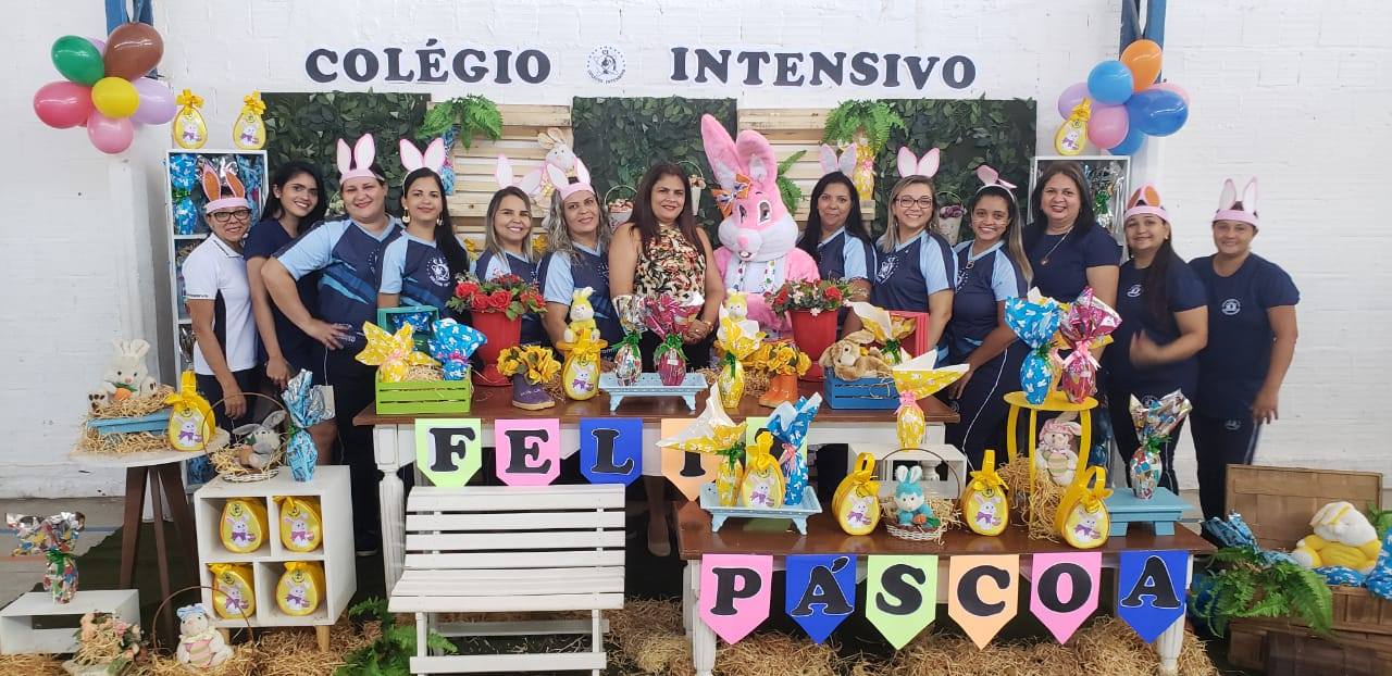 Equipe do Colégio Intensivo reunida em evento pedagógico da escola, com o nome do colégio ao fundo