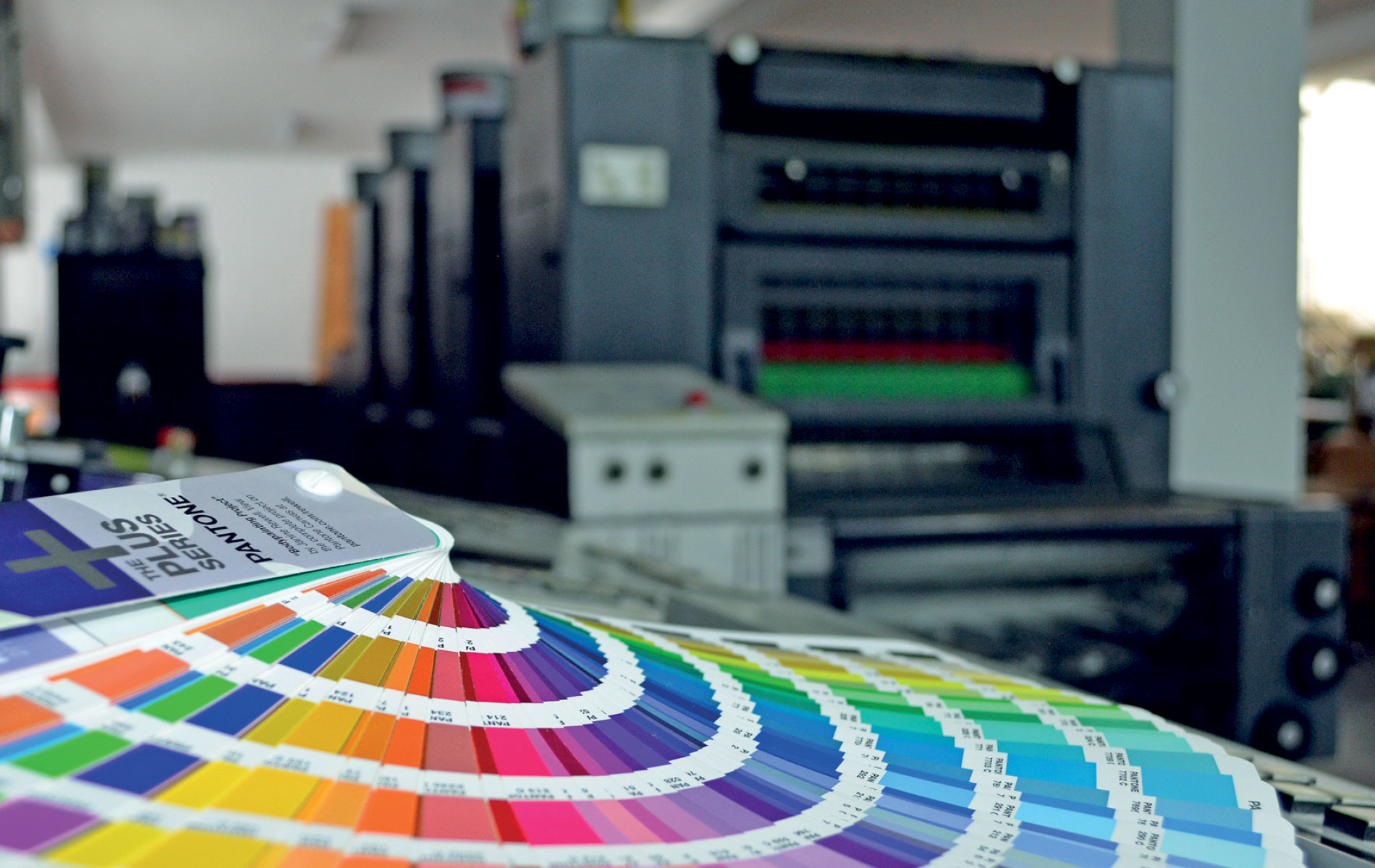 Guía de colores Pantone junto a máquina de impresión offset, control de calidad de color en Digital Center