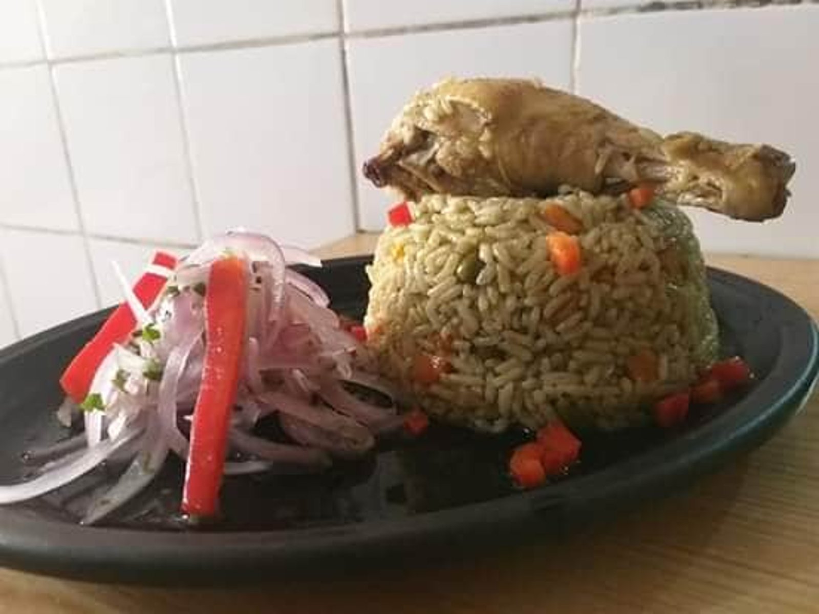 Arroz con pollo a la tarapotina, servido con pierna de pollo entera y ensalada criolla de cebolla y ají