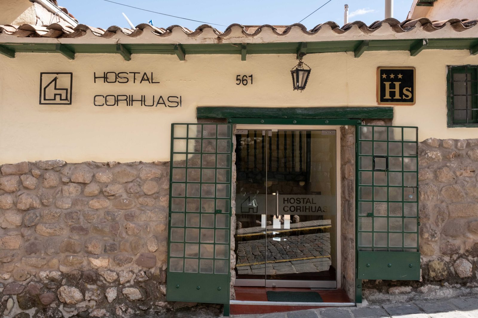 Fachada de piedra y portón verde del Hostal Corihuasi en Calle Suecia 561, Cusco, con su categoría de 3 estrellas