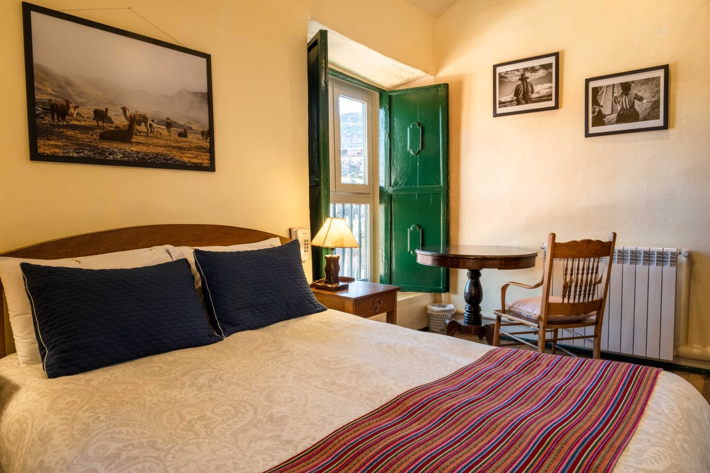 Habitación con balcón de postigos verdes del Hostal Corihuasi, con vista a los tejados de Cusco y textil andino sobre la cama