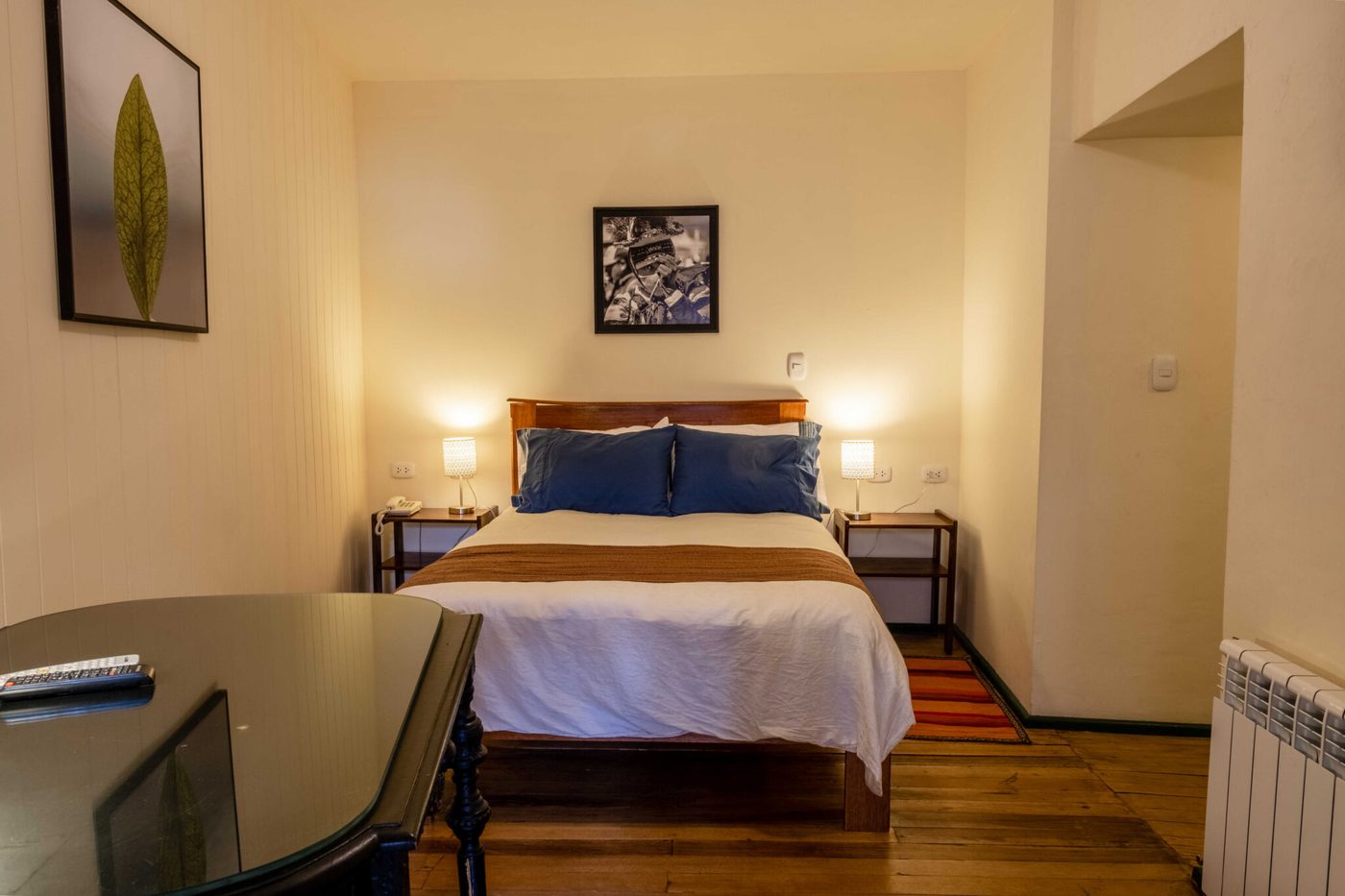 Habitación clásica del Hostal Corihuasi con cama matrimonial, veladores con lámparas y fotografía andina en la pared