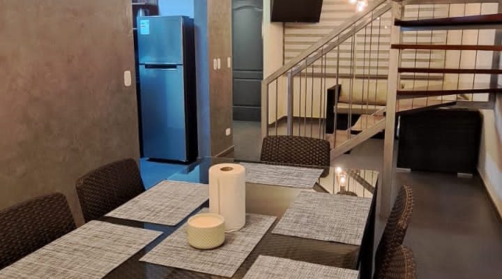 Sala comedor de uno de los departamentos del Hostal Elixer, con mesa para varias personas, sillones y luces cálidas