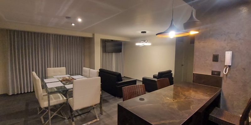 Departamento tipo casa del Hostal Elixer con cama matrimonial, mesa redonda de vidrio y sillas de mimbre junto a la ventana