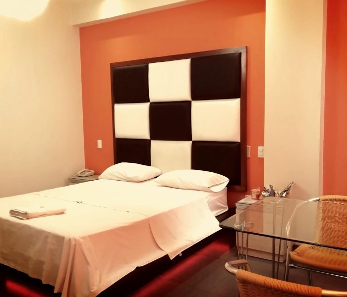 Habitación Matrimonial del Hostal Elixer con cabecera acolchada en negro y naranja, cama tendida y cortinas junto a la ventana