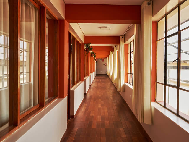 Pasillo de habitaciones del hostal con piso de madera y cortinas