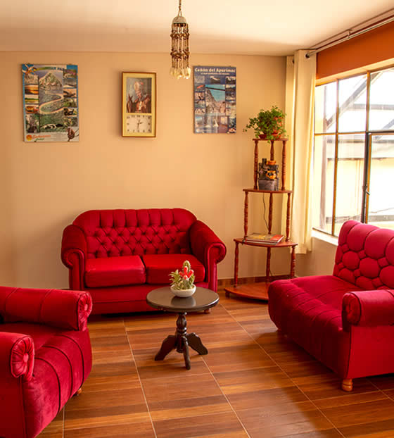 Segunda sala de estar del hostal con sofás rojos y ventanal luminoso