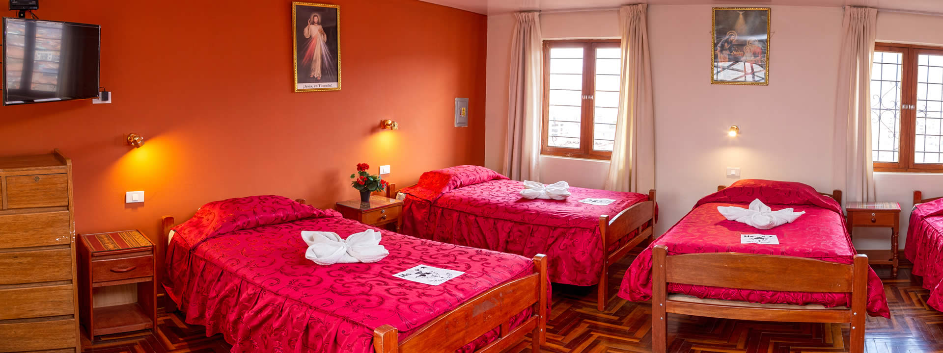 Habitación Doble del Hostal Santa Rosa de Lima con dos camas y cobertores rojos junto a ventana