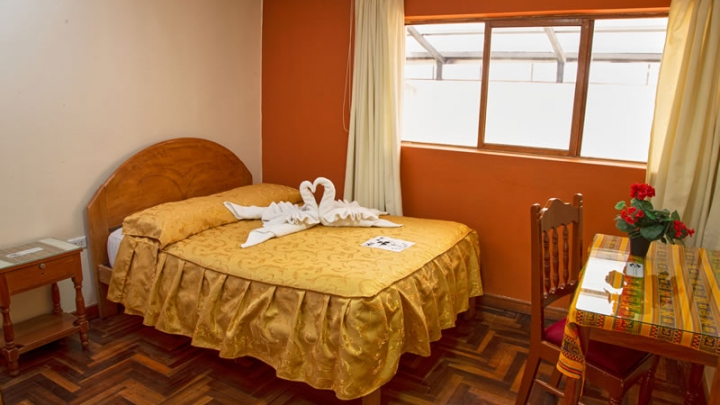 Habitación Matrimonial del Hostal Santa Rosa de Lima con cama doble, cobertor dorado y toallas decorativas