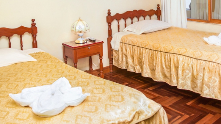 Habitación Triple del Hostal Santa Rosa de Lima con camas de cobertor dorado, piso de madera y velador