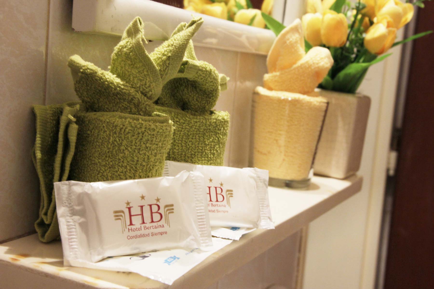 Detalle de amenities del Hotel Bertaina: jabones de tocador con la marca HB y la leyenda Cordialidad Siempre, junto a toallas dobladas