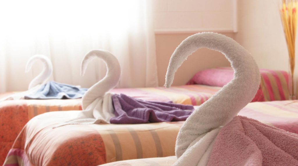 Fila de camas del Hotel Bertaina con toallas dobladas en forma de cisne de distintos colores