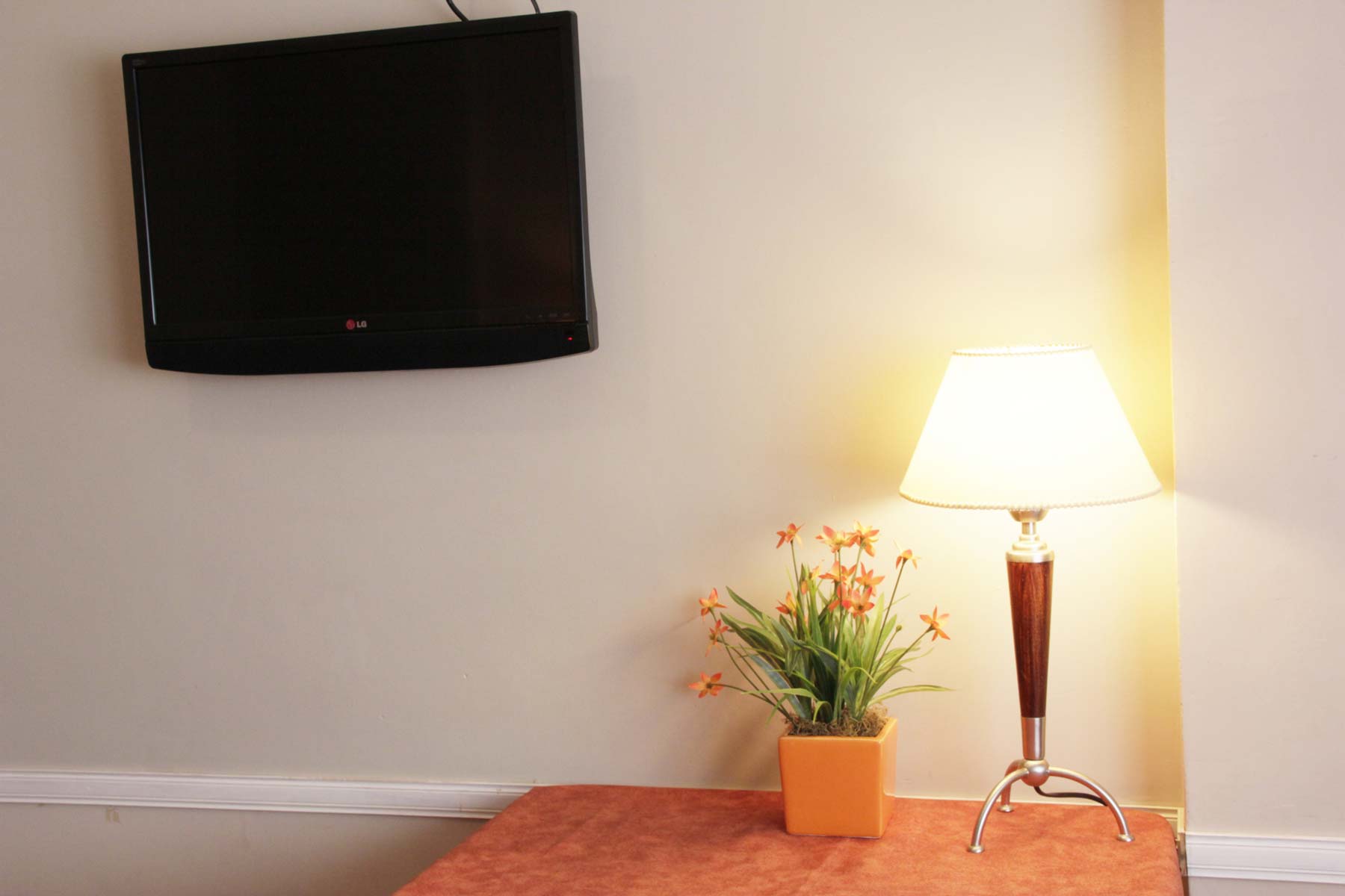 Televisor LG y velador con flores en una habitación del Hotel Bertaina