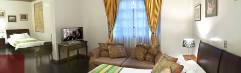 Habitación Superior del Hotel Cuenca con sala de estar, ventanal con cortinas doradas y televisión
