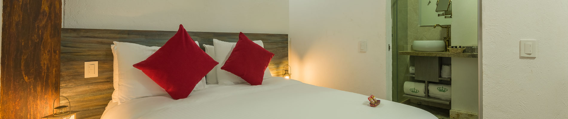 Habitación Estándar del Hotel Getsemaní Luxury con cama vestida en blanco y cojines rojos