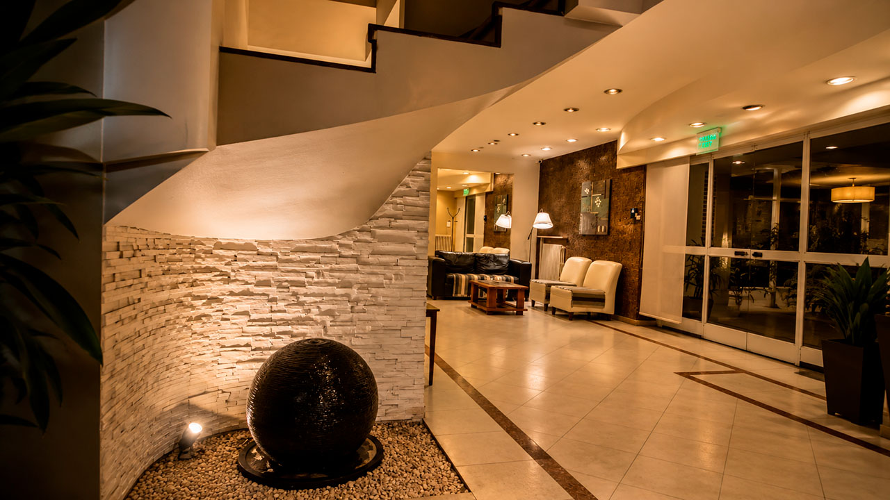 Detalle del lobby del Hotel Hernandarias con escalera curva, pared de piedra y fuente decorativa