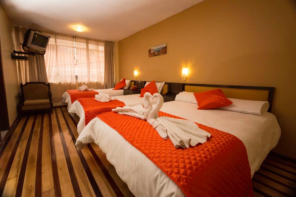 Habitación Triple del Hotel Riobamba Inn con tres camas, televisor y piso de madera, ideal para familias