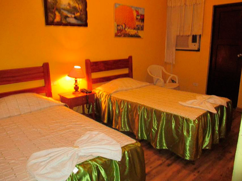 Habitación Doble del Hotel Tarapoto Inn con dos camas cubiertas en satín verde y silla junto a la ventana