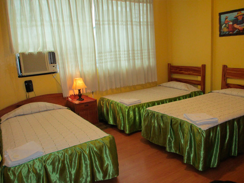Habitación Triple del Hotel Tarapoto Inn con tres camas cubiertas en satín verde y cortinas claras