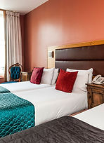 Habitación del International Prestige Hotel con ropa de cama blanca y cojines en tono vino