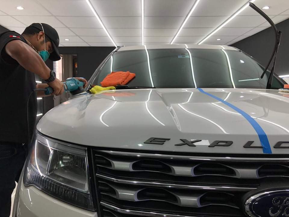 Técnico de Jaguar Car Detailing puliendo con máquina el capó de una camioneta blanca en el taller