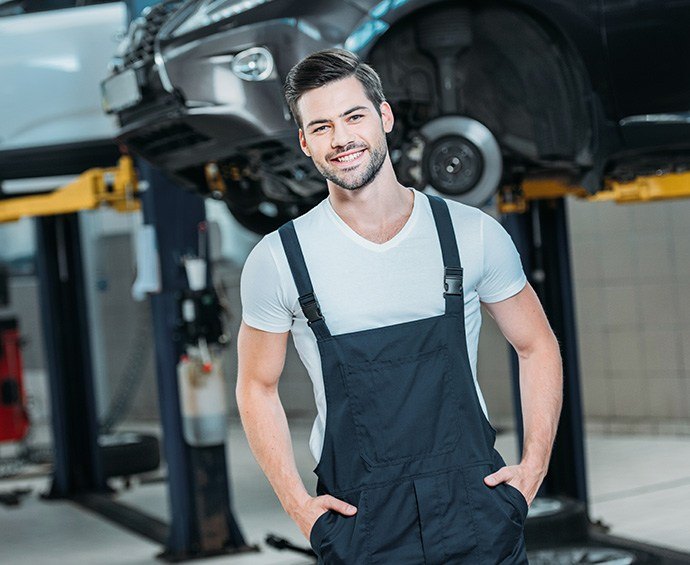Mecánico sonriente junto a vehículo elevado durante mantención en taller