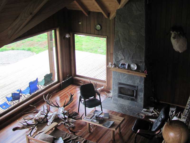 Living con revestimiento en madera y chimenea de piedra en una casa construida por Muebles HZ