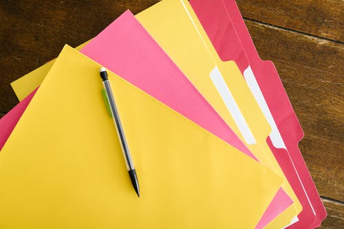 Carpetas de colores rosa y amarillo con un lápiz encima