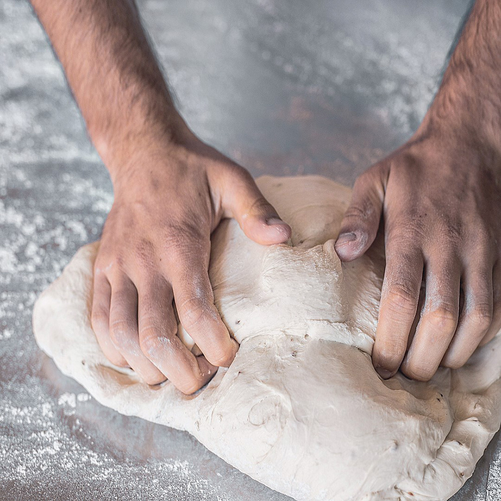Manos de panadero amasando y dando forma al pan sobre la mesa de trabajo