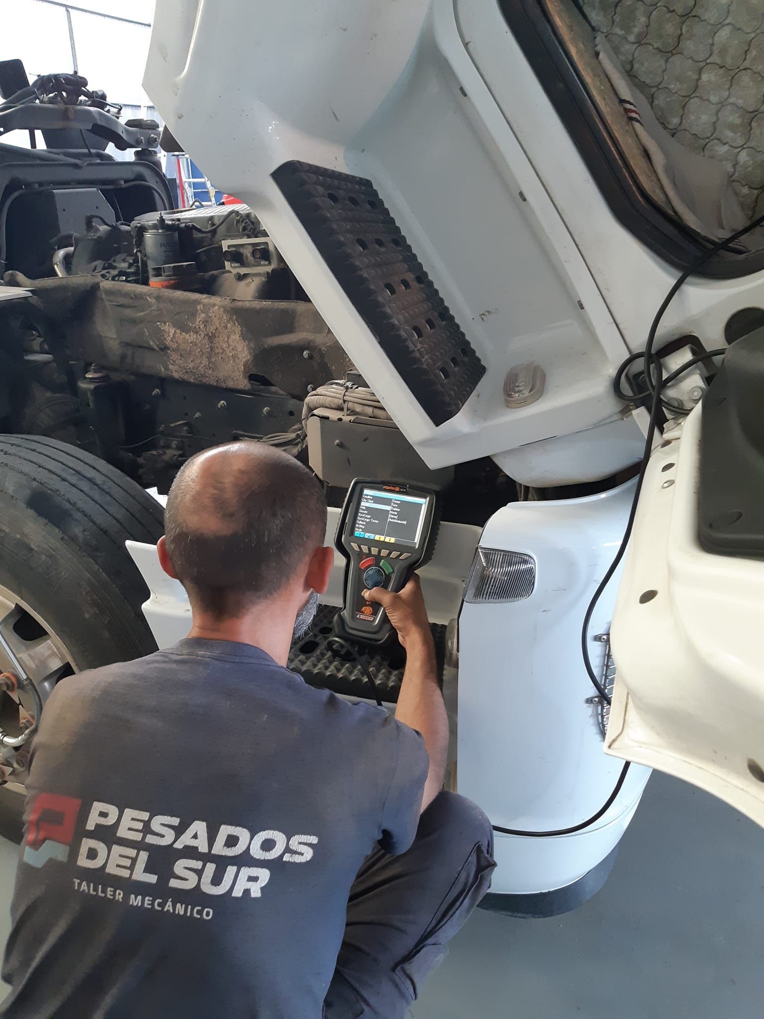 Mecánico de Pesados del Sur, con el uniforme de la marca, revisando el chasis de un camión con un scanner de diagnóstico computarizado
