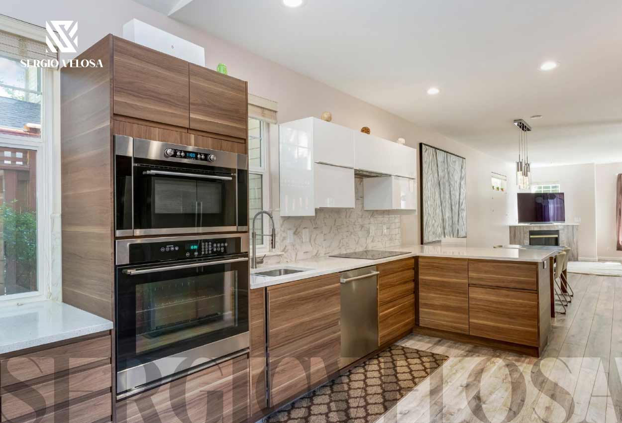 Cocina integral en madera de nogal con isla, cubierta blanca y electrodomésticos empotrados, fabricación de Sergio Velosa