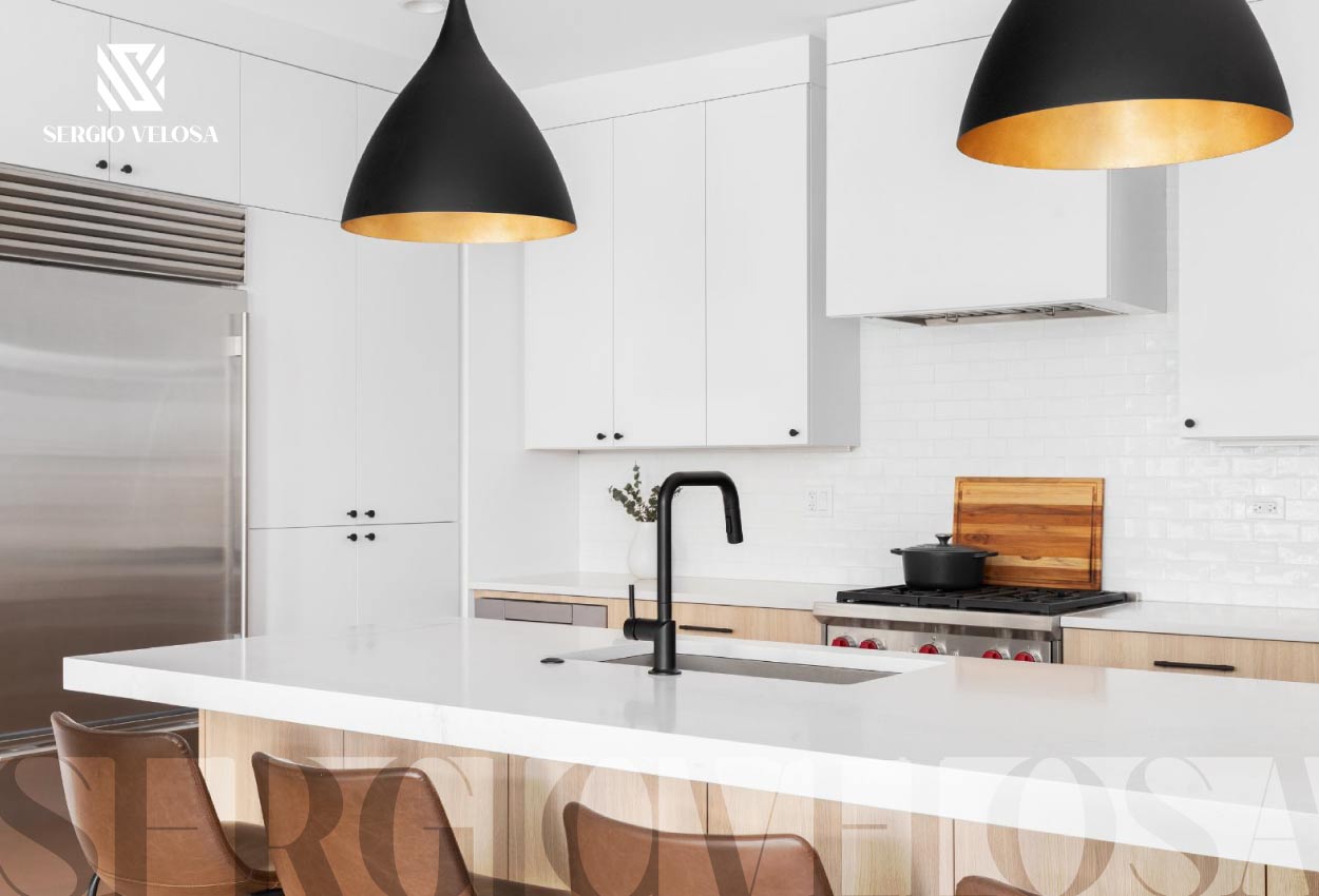 Cocina integral blanca con isla, lámparas colgantes negras y sillas de cuero, fabricación a la medida