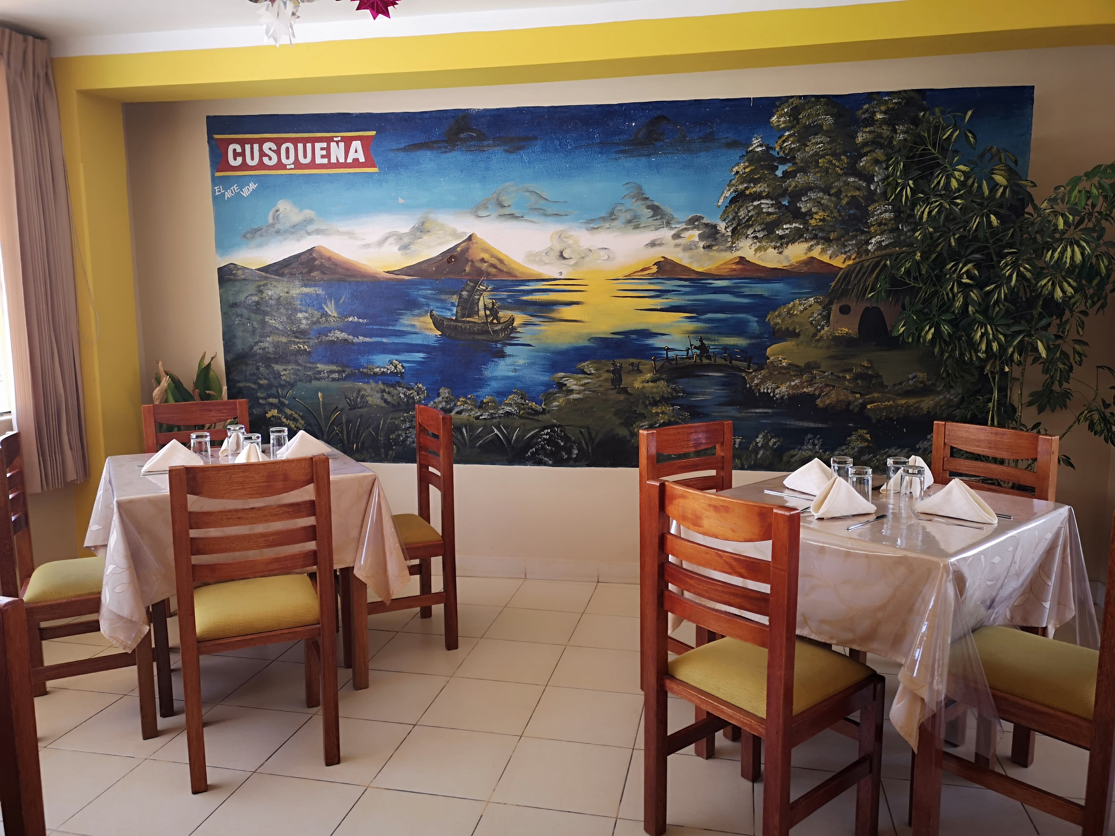 Comedor de Restaurant Sombreritos con mural pintado a mano del lago Titicaca y mesas tendidas para el servicio